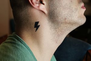 A man in a green shirt having a thunderbolt tattoo on his neck.