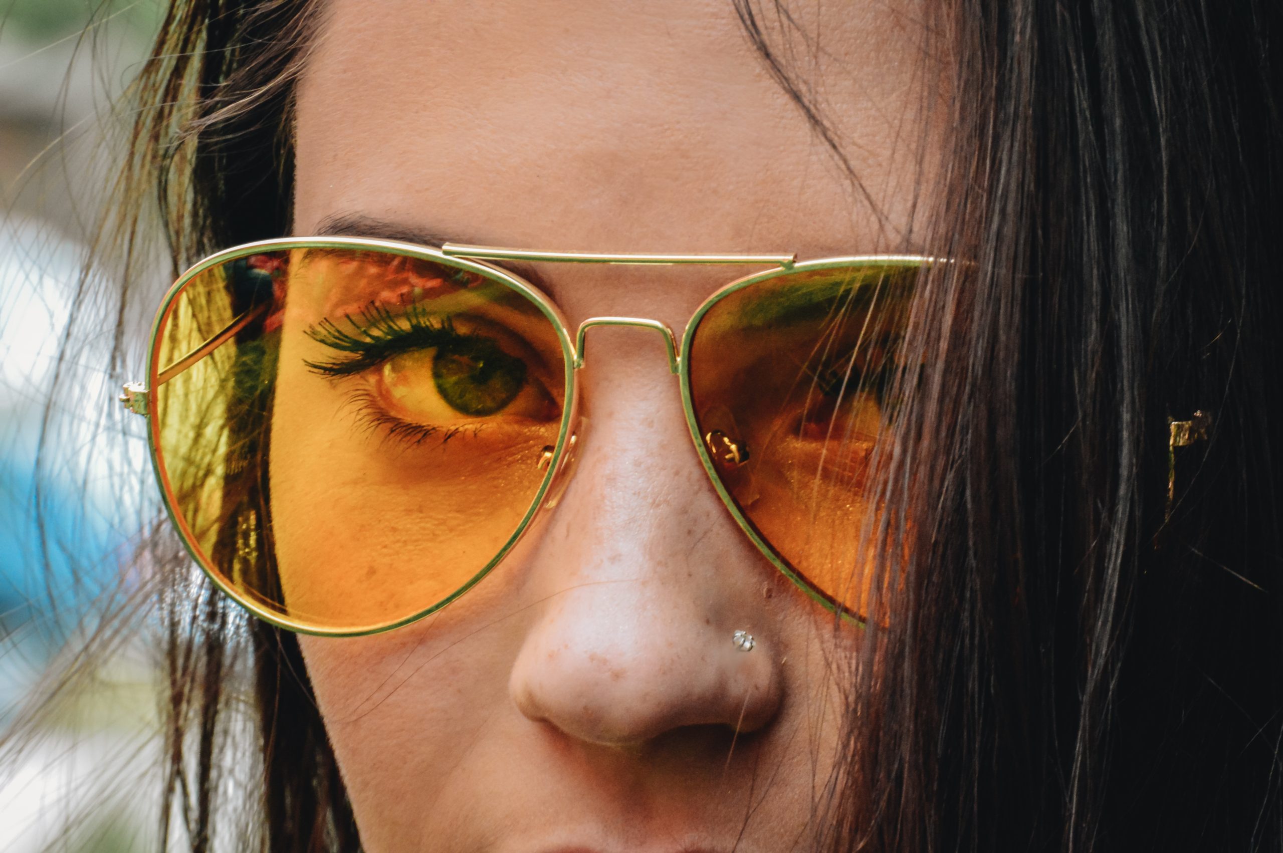 Woman wearing gold framed aviator sunglasses with a nose pin.