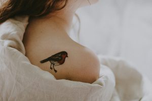 Woman with bird tattoo in shoulder laying on white surface