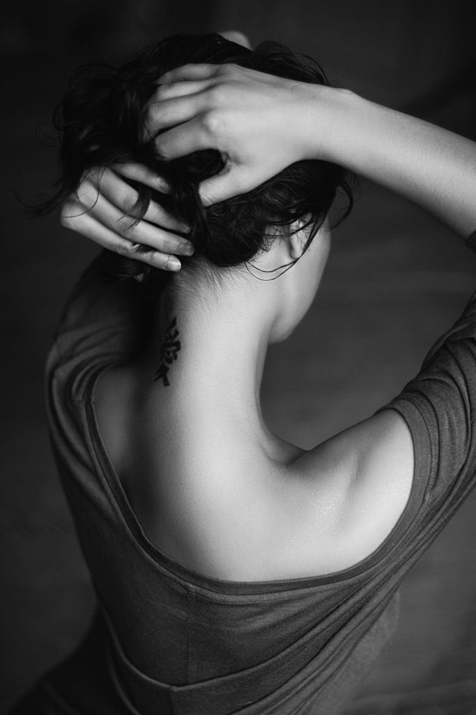 Woman holding her hair up with a tattoo on her neck.