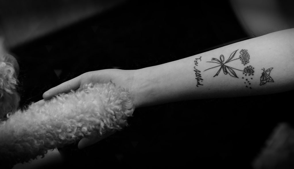 Black and white photo of a person holding a dogs paw and a dandelion tattoo.