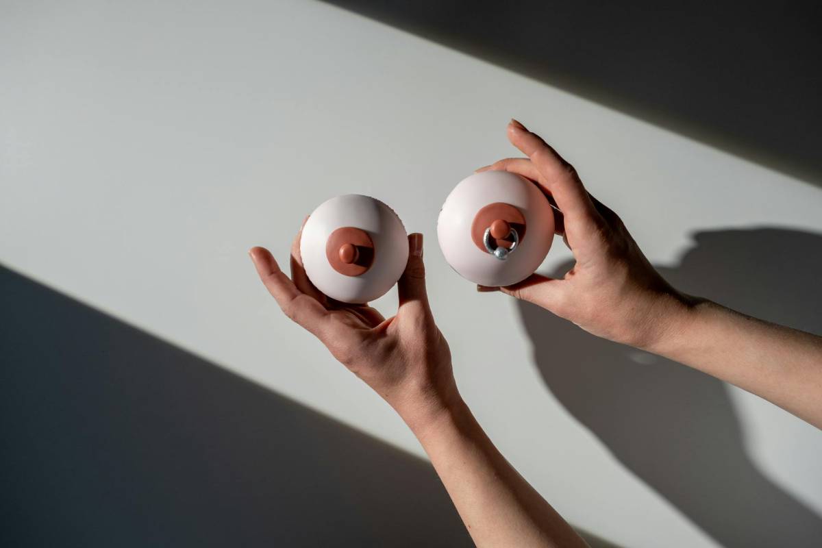 Person holding two cupcakes in a shape of nipples with a piercing