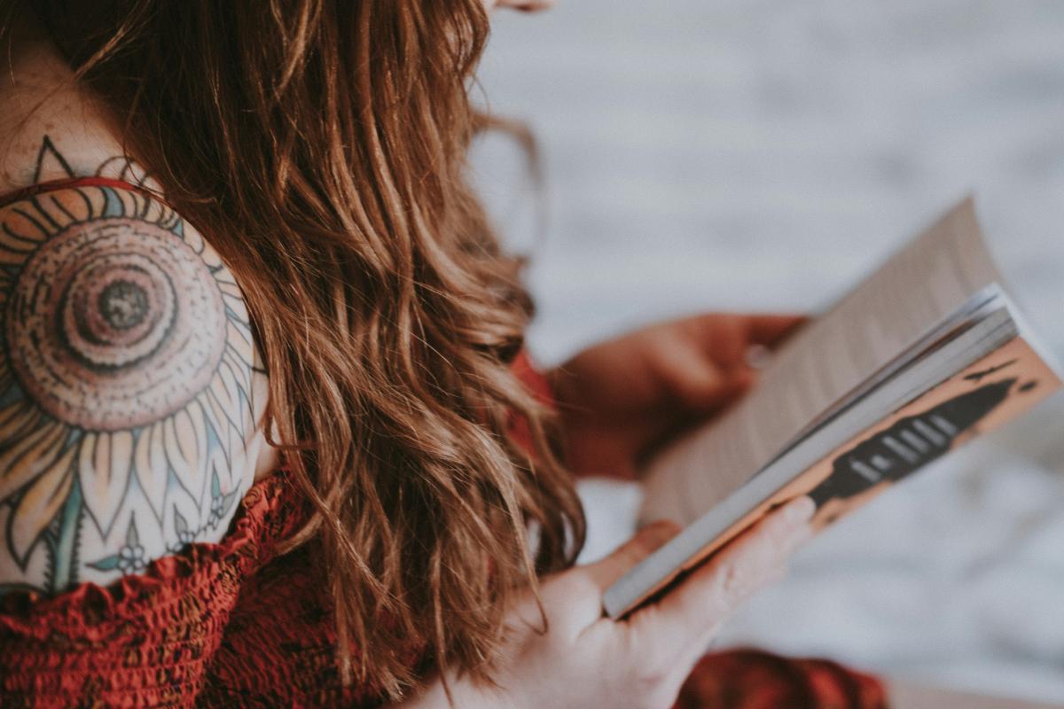 Woman in a red dress, reading a book, with sunflower tattoo on her shoulder.