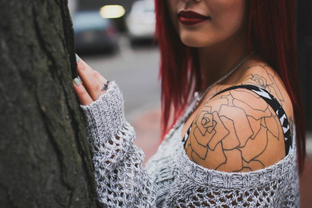 Woman leaning on a tree with a white net blouse and shoulder tattoo