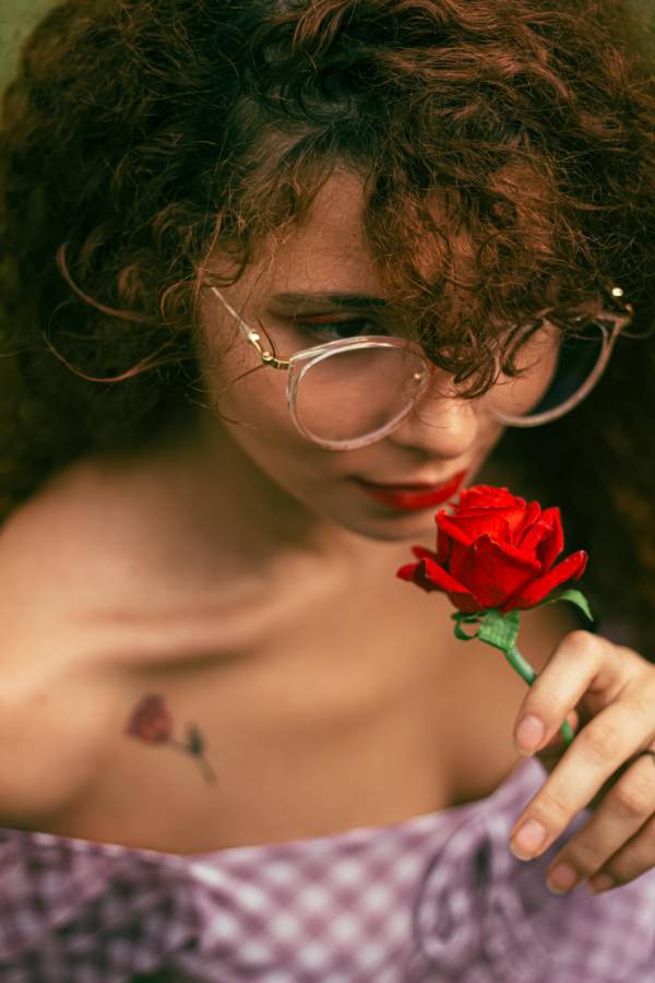 Woman with curly hair and glasses holding a rose with rose tattoo